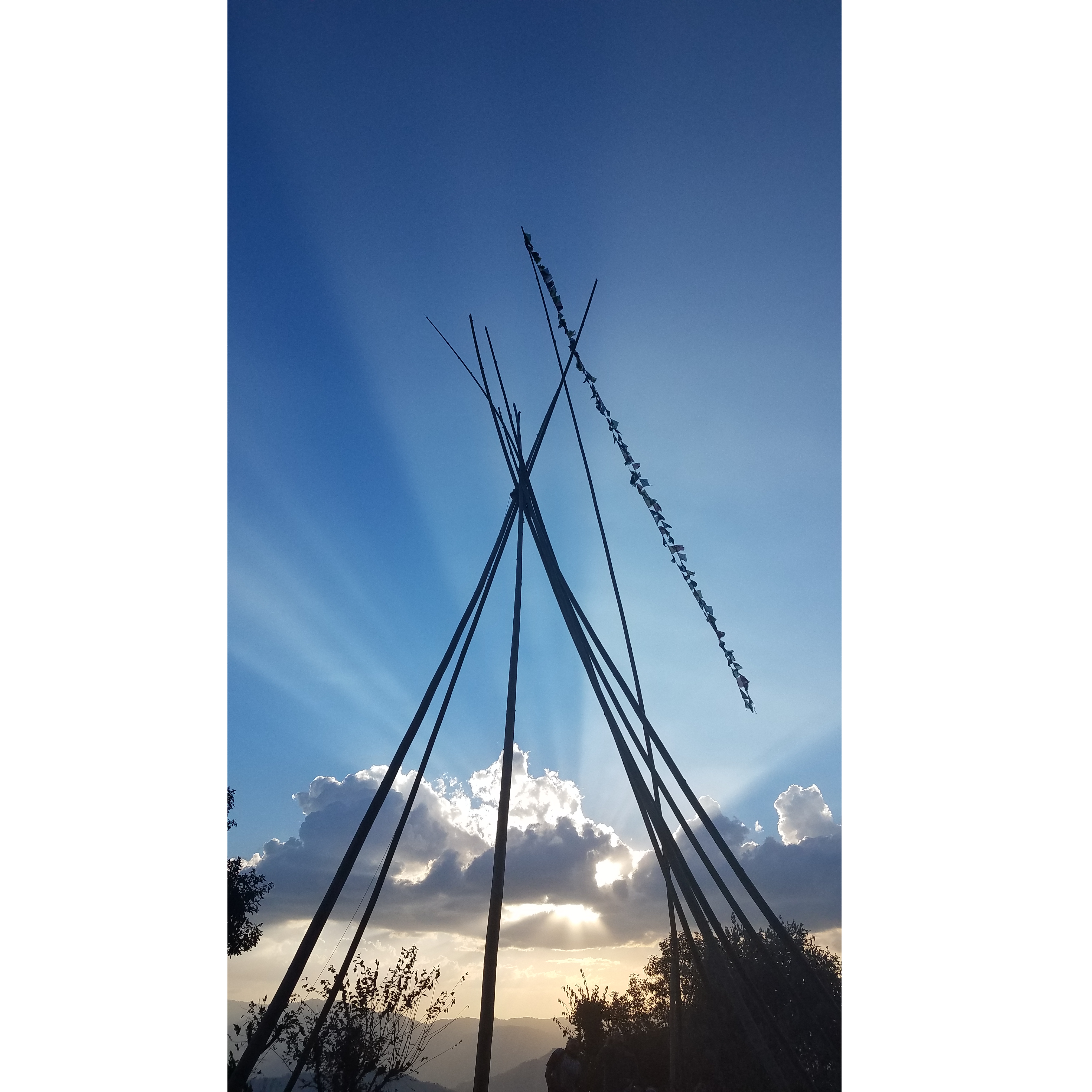 Sun rays shining on the skeleton of our new teepee common space, with prayer flags trailing.